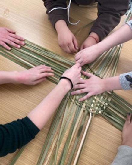 Photo of various hands working to weave a square